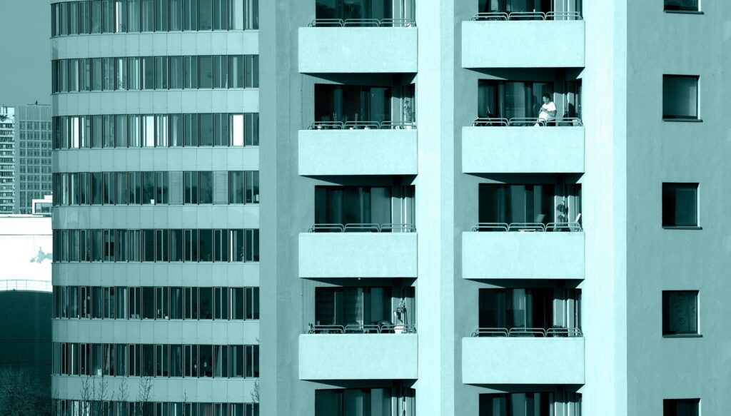 Modern high-rise condominium balconies and windows rise in a teal-tinted urban skyline, with a few residents visible.